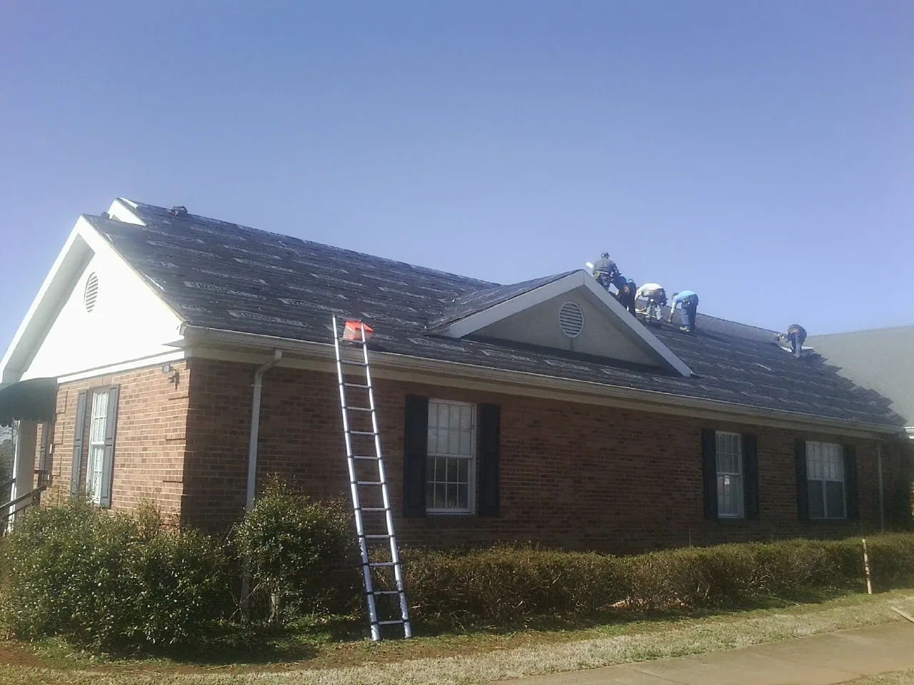 Crew tearing shingles off a brick ranch roof with a ladder set — Metal Roof Repair work by our crew in Pamplin