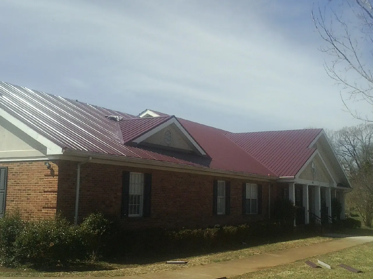 Red metal roof with gabled entries on a long brick building, from a Hail Damage Roof Repair job in Pamplin