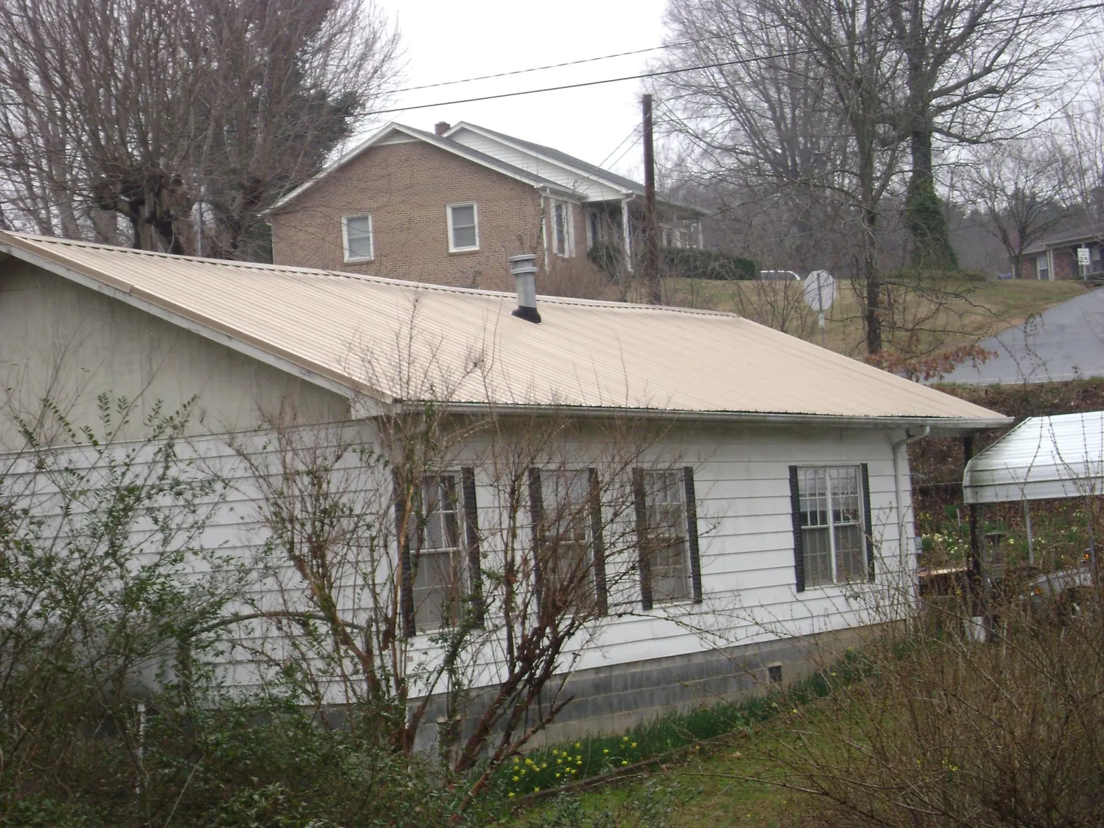 Tan metal roof on a white sided house set into a hillside — Commercial Roofing by Roofing Brothers in Pamplin