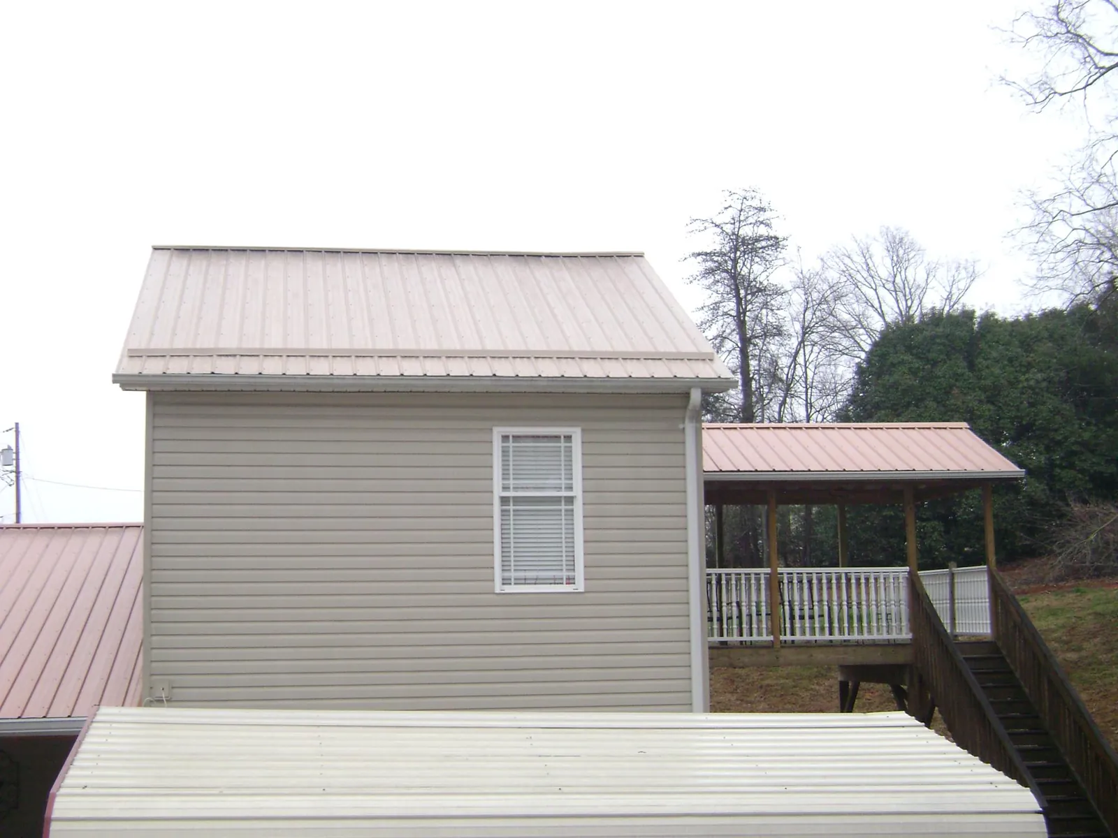 Tan metal roofs on a two story addition and attached porch, from a Roof Replacement job in Pamplin